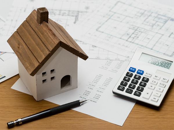 電卓とペンと茶色い屋根の家の模型